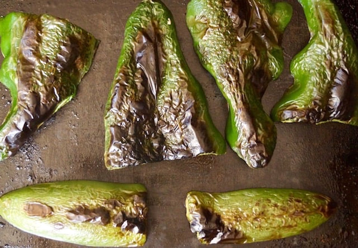 Charred halved poblano peppers and jalapeno peppers on a sheet pan.