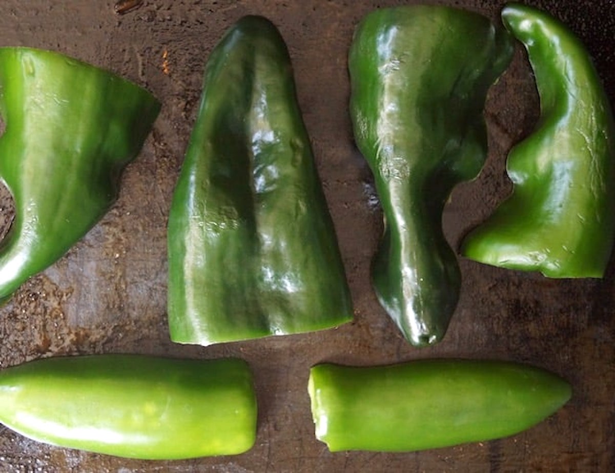 Raw halved poblano peppers and jalapeno peppers on a sheet pan.