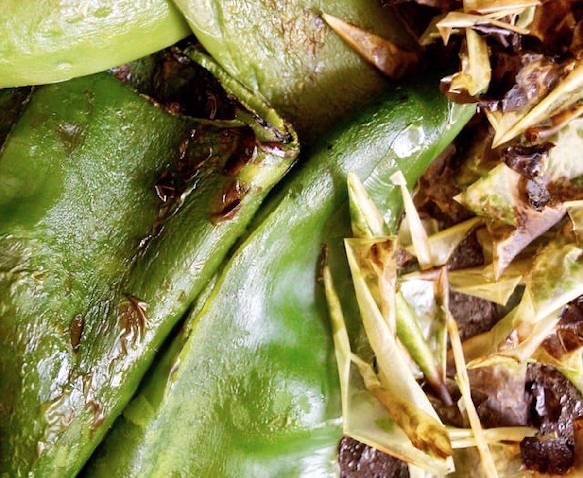 roasted and peeled pbolano peppers with pile of skins next to them