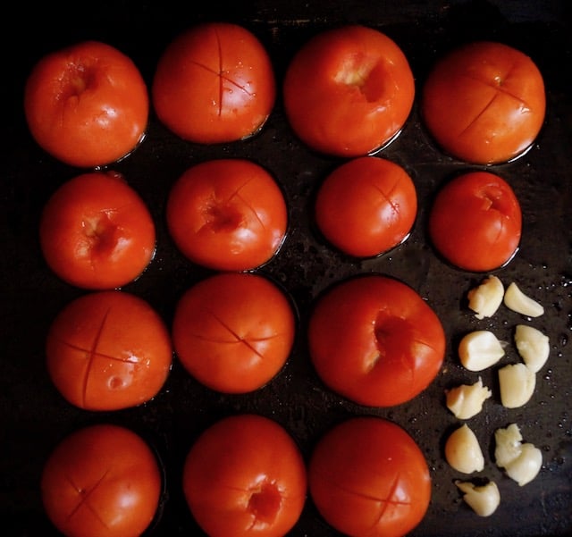 several tomato halves on baking sheet with garlic cloves