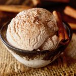 Scoop of beautiful cinnamon ice cream with cinnamon sprinkled on top and with a cinnamon stick in the bowl.