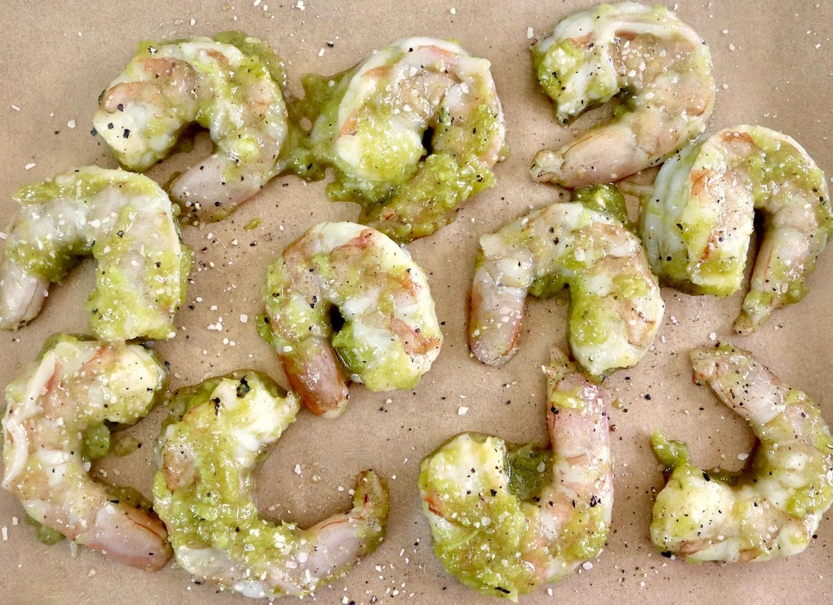 Several raw shrimp on a parchment-lined sheet pan with hatch green chile marinade.