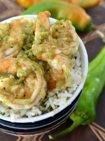 White bowl with rice and shrimp with green sauce on top.
