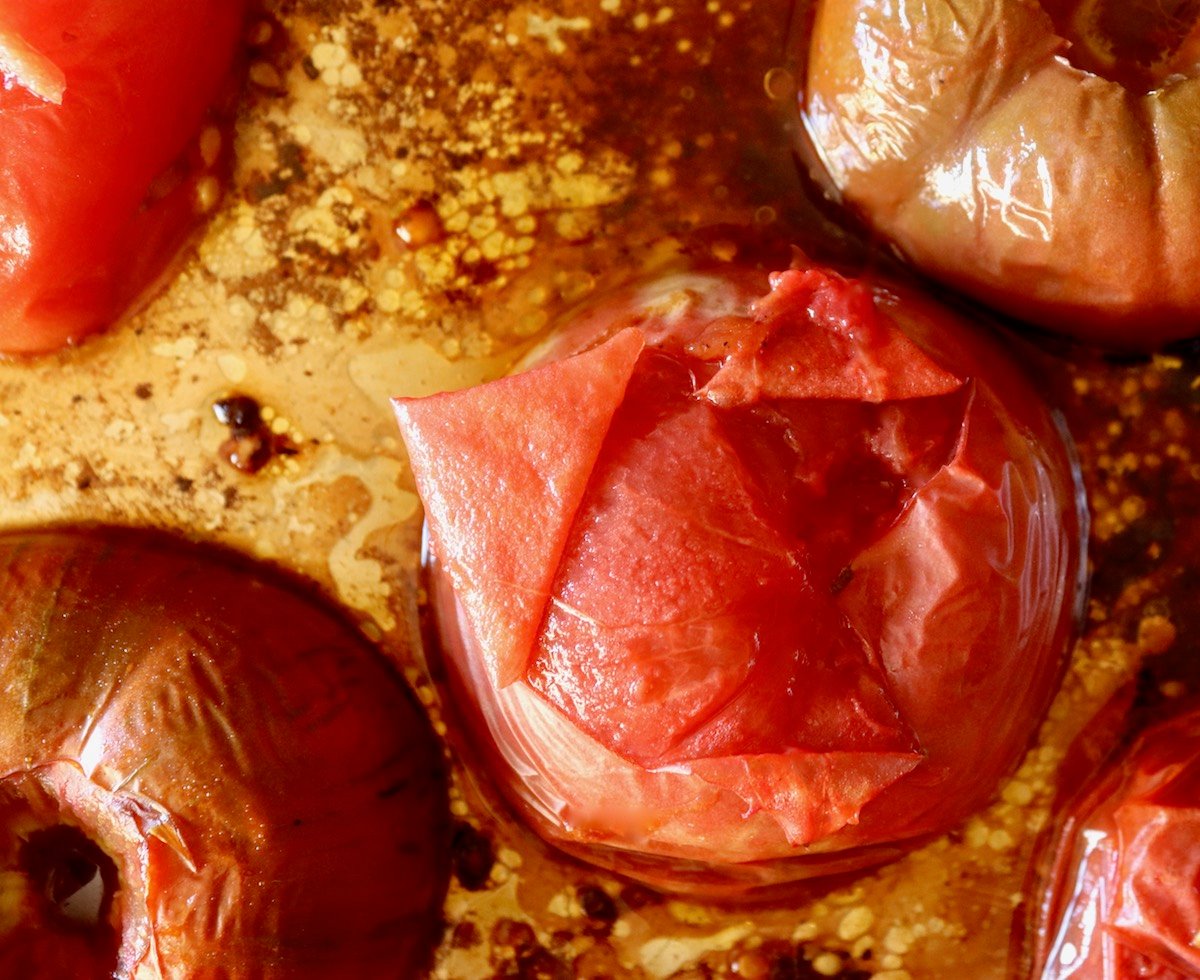 Roasted tomato on a sheet pan with skin peeling off from cut lines on the bottom of the tomato.