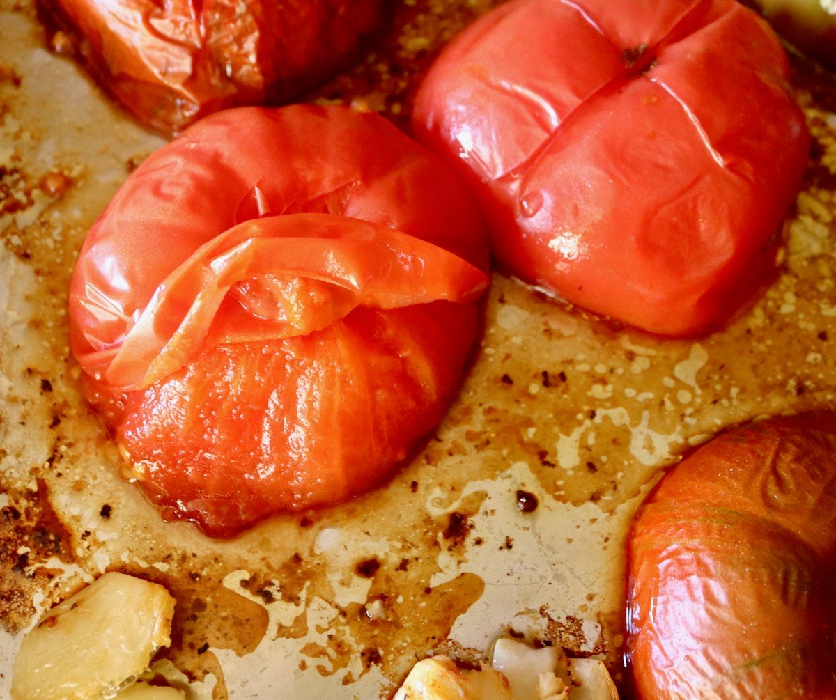 Roasted tomato on a sheet pan with skin peeling off from root.