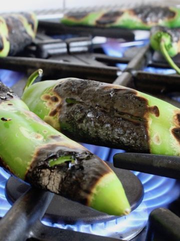 A few hatch chiles on burners with a hight blue flame.