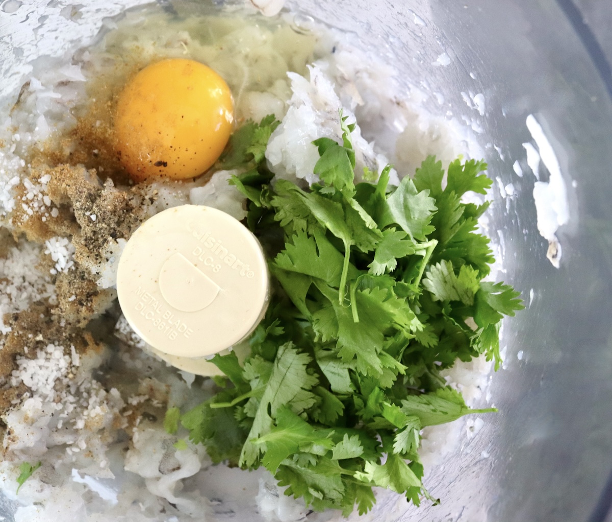 Shrimp paste with raw egg and cilantro in food processor bowl.