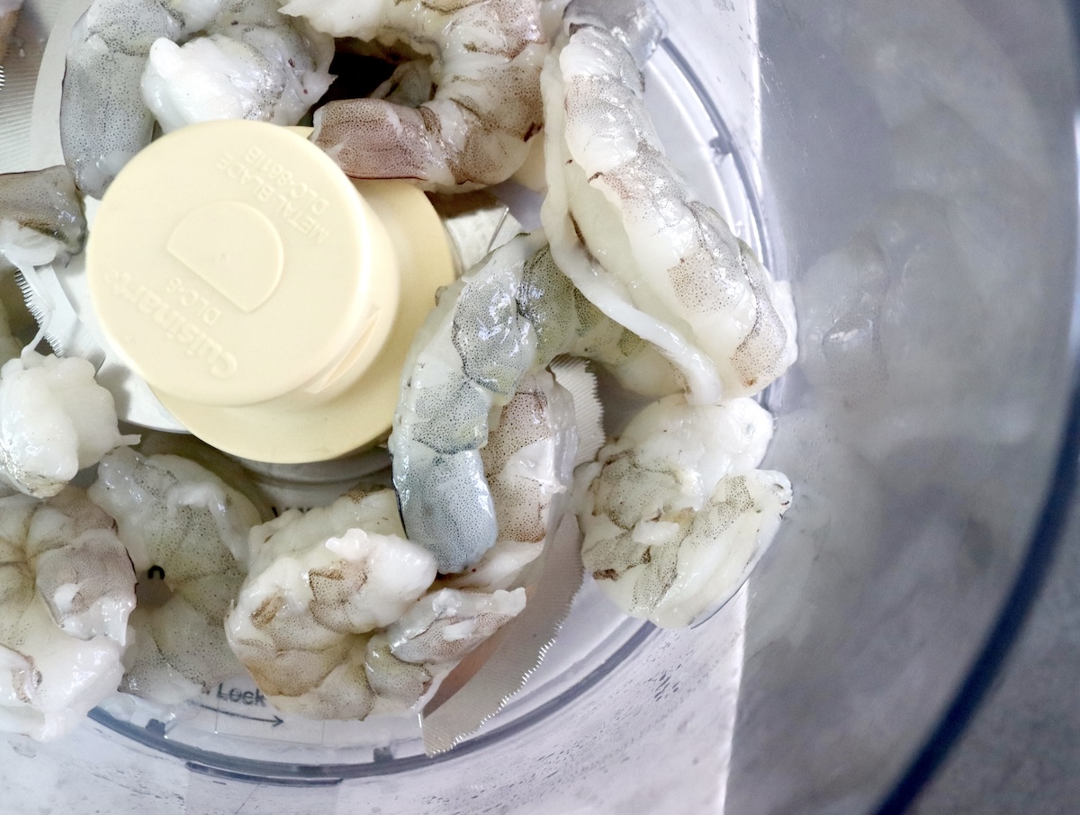 Raw shrimp in food processor bowl.
