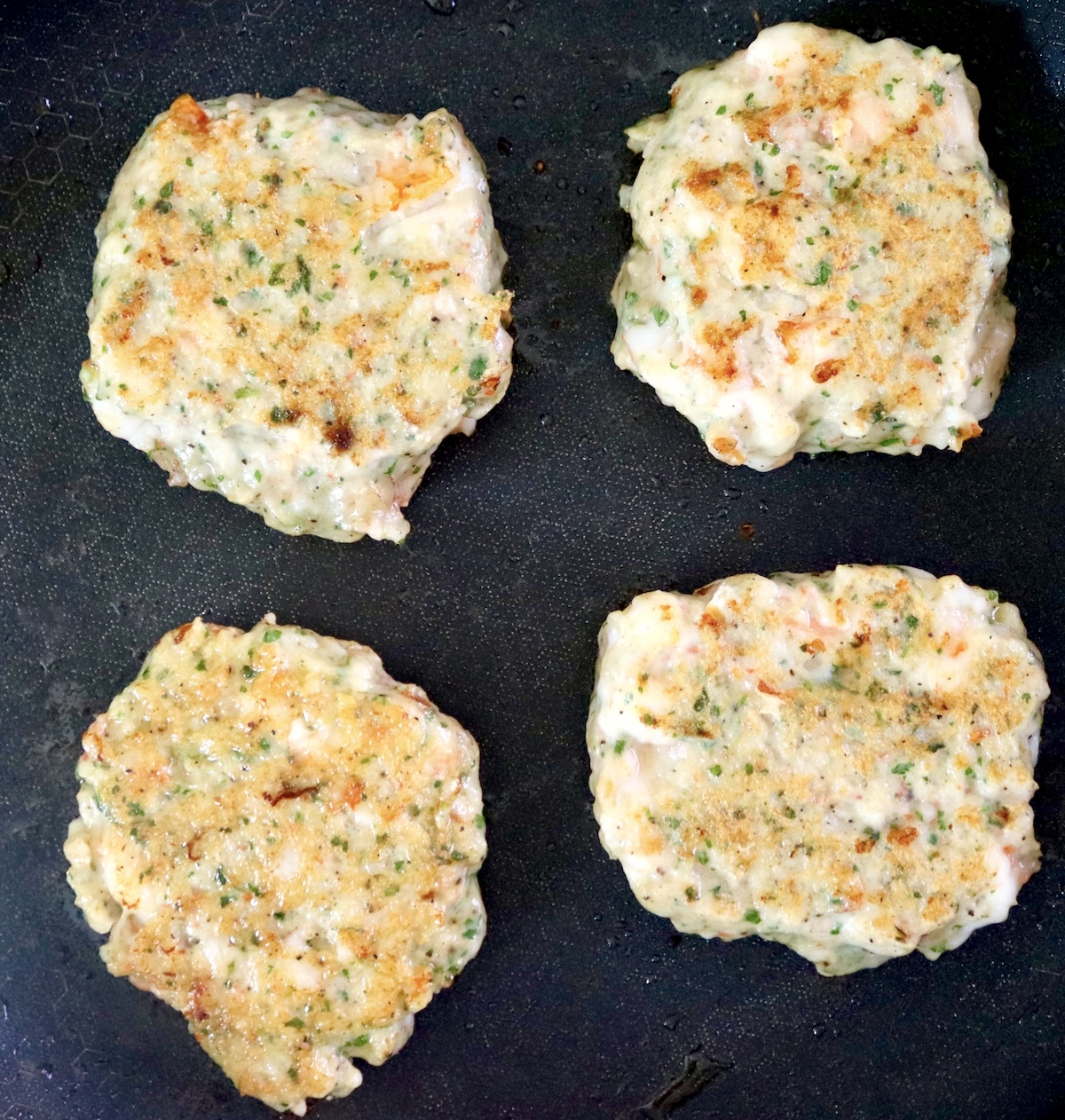 4 cooked pink-ish shrimp burgers in a saute pan.