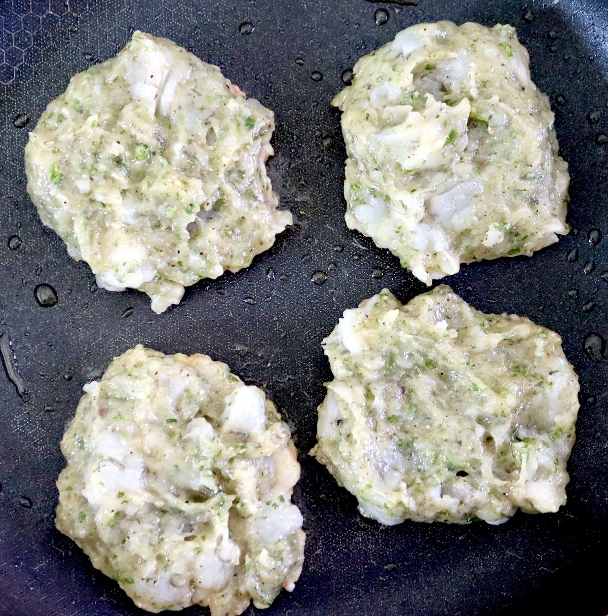 4 raw shrimp burgers in a saute pan.