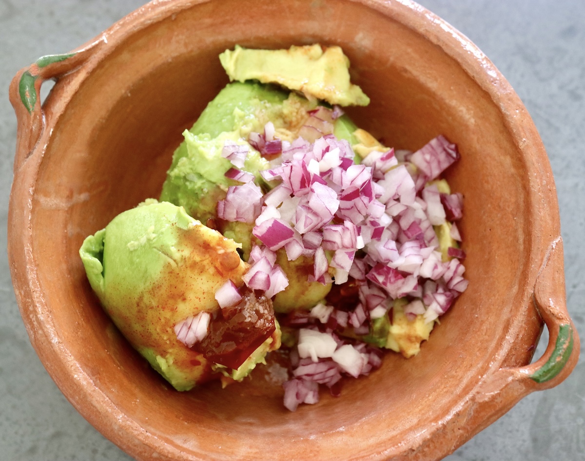 Avocado with diced red onion and adobo sauce in a terra cotta bowl. 