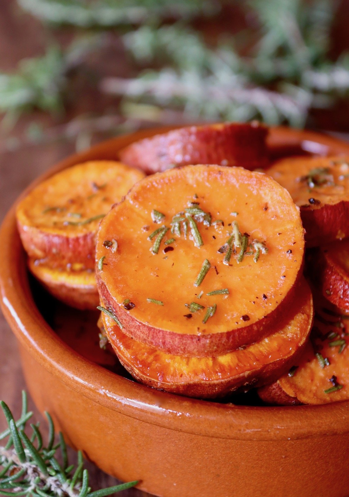 Terra cotta round dish with sweet potato slices with chopped rosemary.