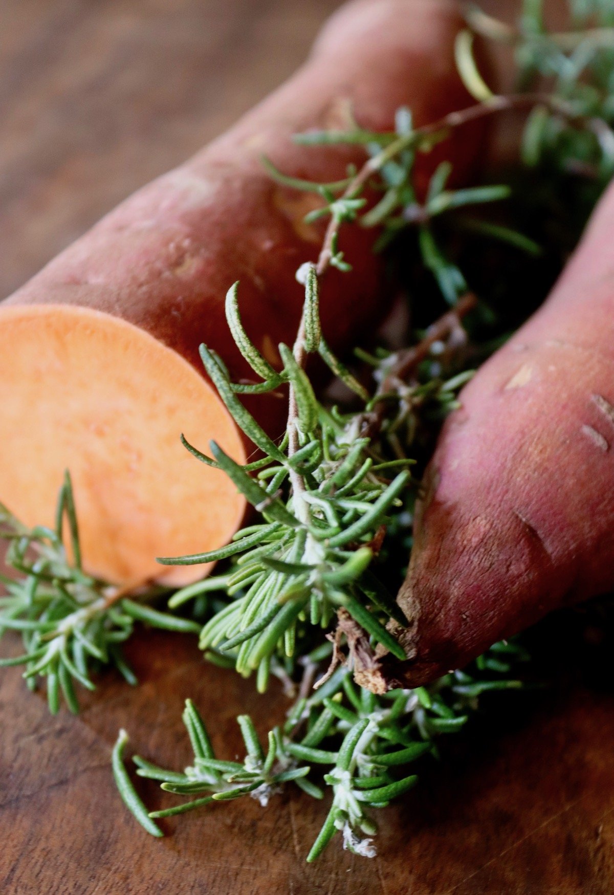 Sweet potato cut in half with sprigs of fresh rosemary, on cutting board.