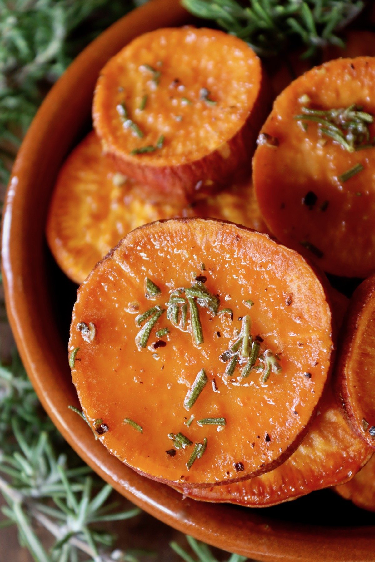 Close up of rosemary sweet potatoes in a round terra cotta dish.