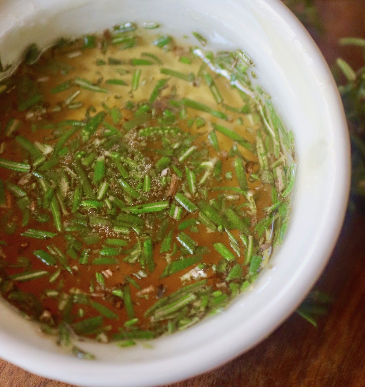 Small white dish with honey and chopped rosemary mixed together.