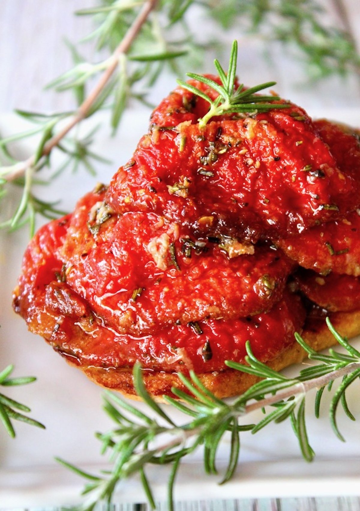 Pile of slow roasted tomato confit with sprigs of rosemary on a white plate.
