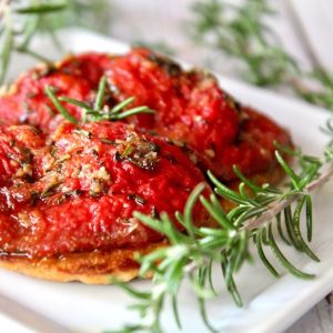 Pile of slow roasted tomato confit with sprigs of rosemary on a white plate.