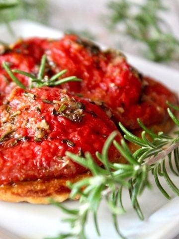 Pile of slow roasted tomato confit with sprigs of rosemary on a white plate.