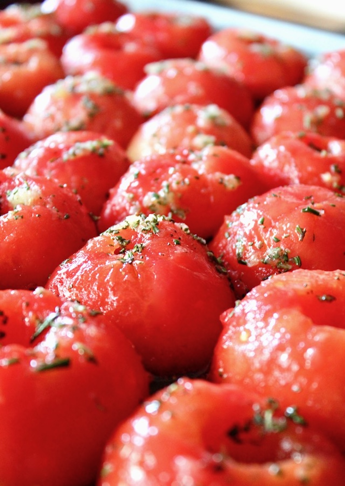 Raw halved and peeled tomatoes with bits of rosemary on a sheet pan,