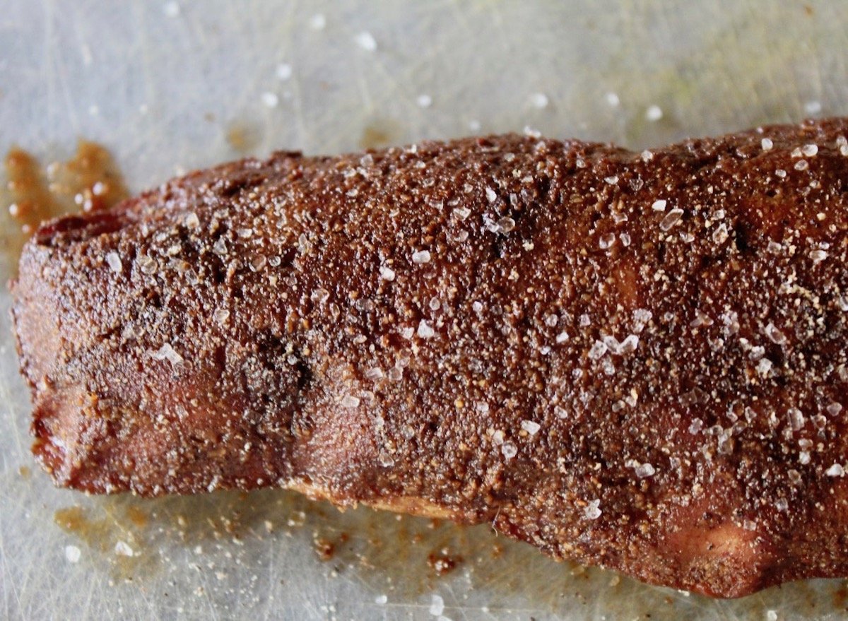 Pork tenderloin with spice rub coating it on parchment paper.