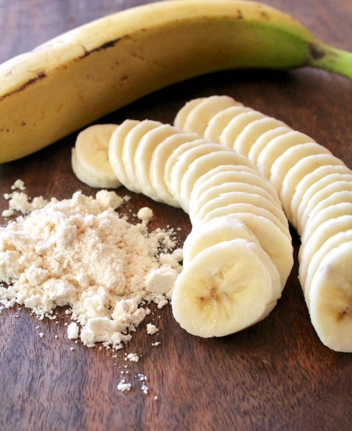 1 whole banana, sliced banana and a small pile of coconut flour - on a dark wood cutting board.