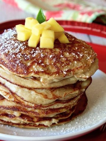 Tall stack of coconut flour pancakes on a white plant that's on a red tray, with pineapple on top.