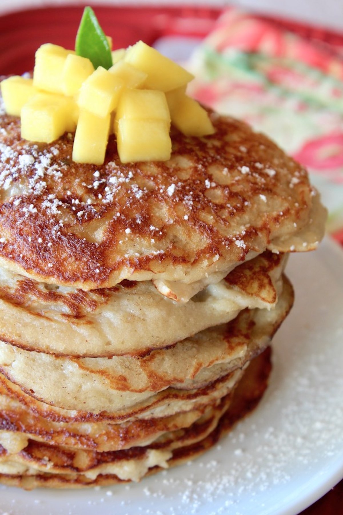 Tall stack of coconut flour pancakes on a white plant that's on a red tray, with pineapple on top.