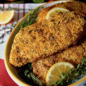 Yellow rimmed bowl full with Air Fryer Gluten Free Lemon Fried Chicken breasts, with lemons in background.