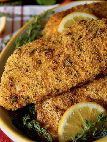 Yellow rimmed bowl full with Air Fryer Gluten Free Lemon Fried Chicken breasts, with lemons in background.