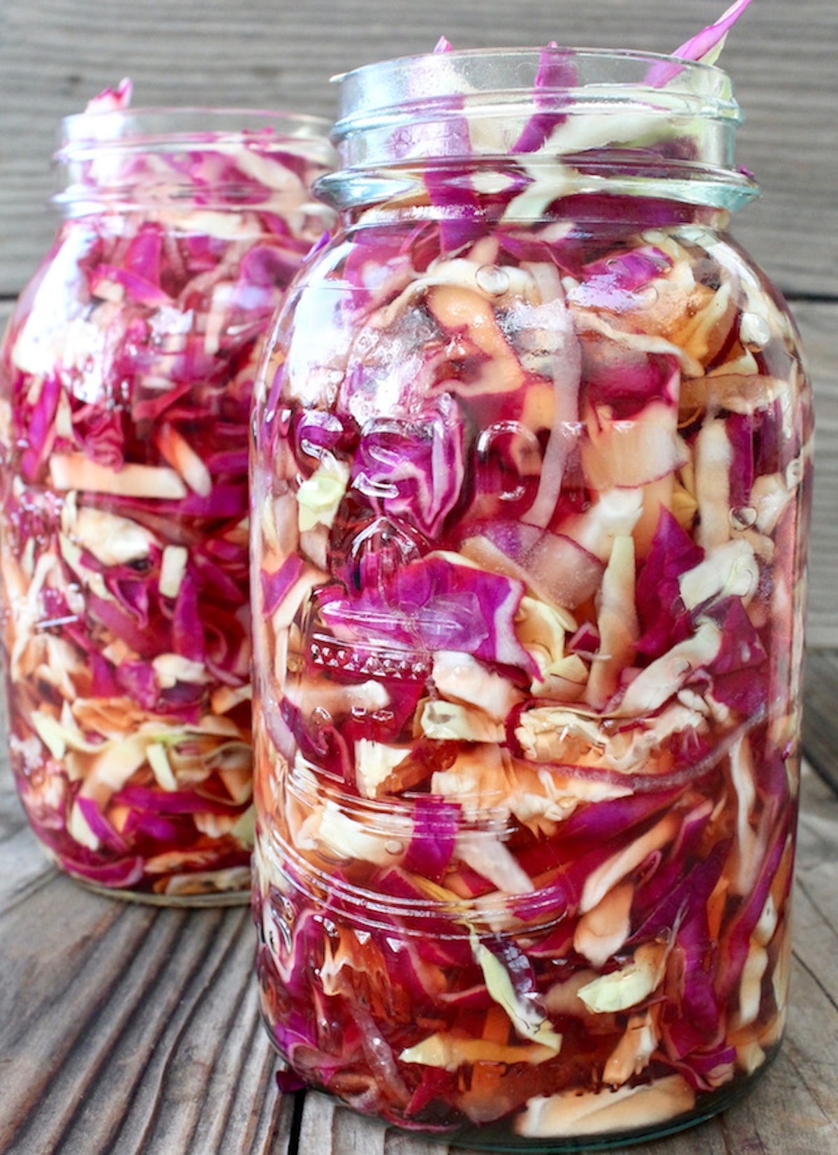 Two jars of marinated thinly sliced purple and green cabbage.