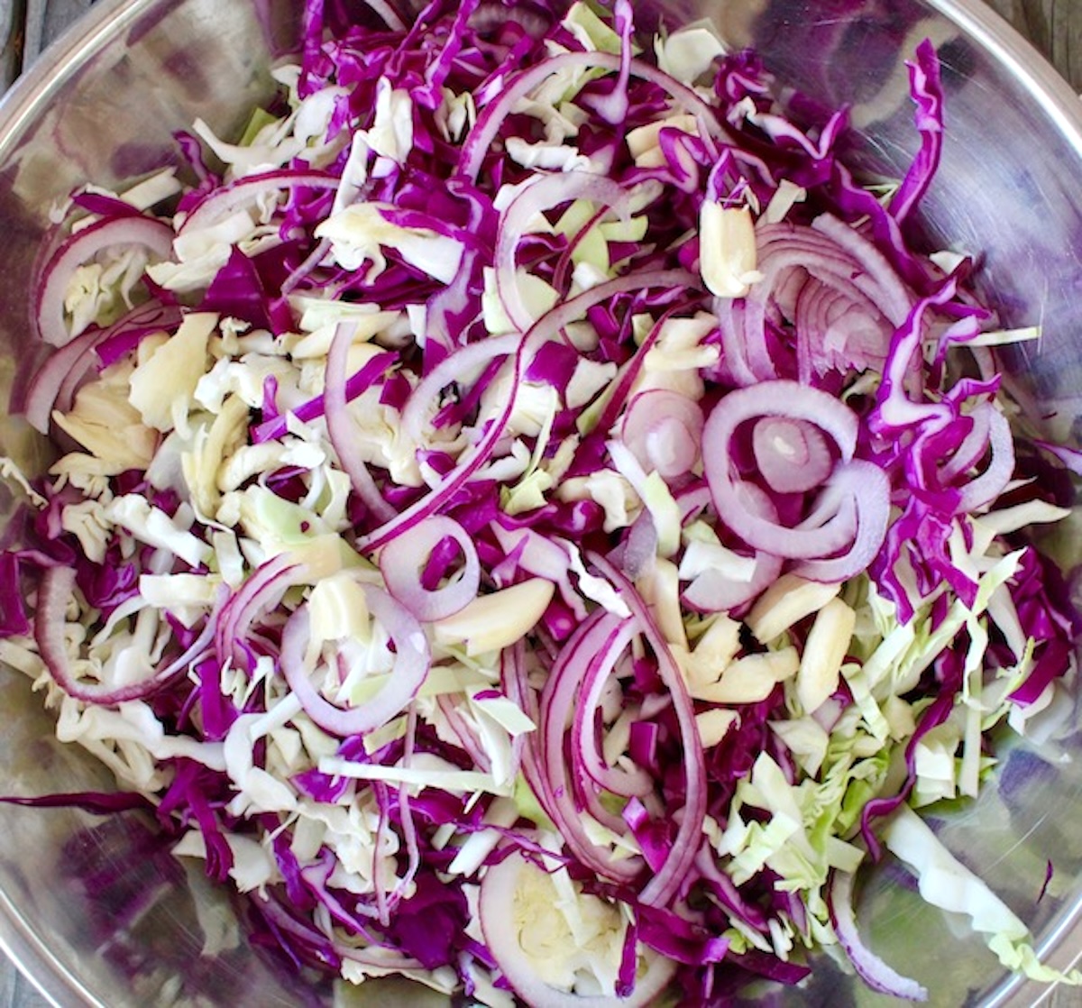 Stainless steel bowl with sliced cabbage and red onion.