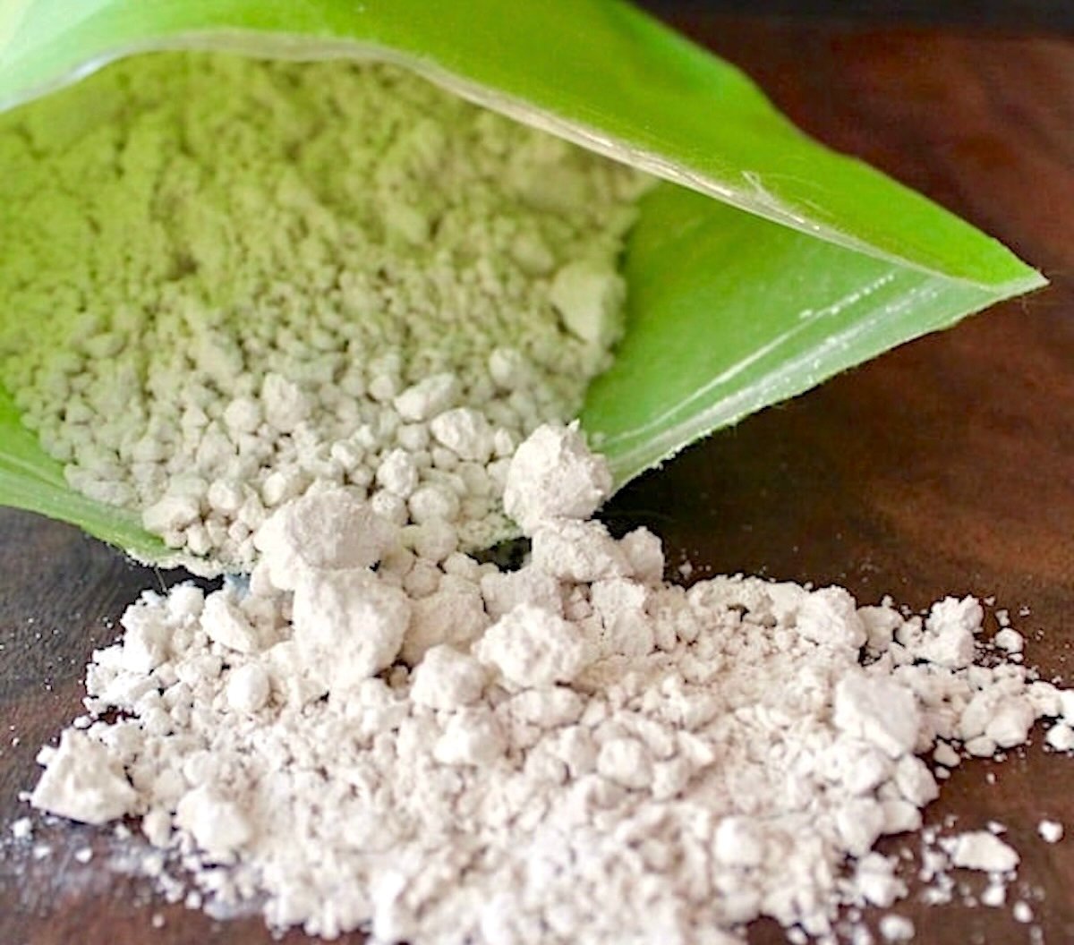 Green bag partially open with chestnut flour pouring out and onto a wooden surface.