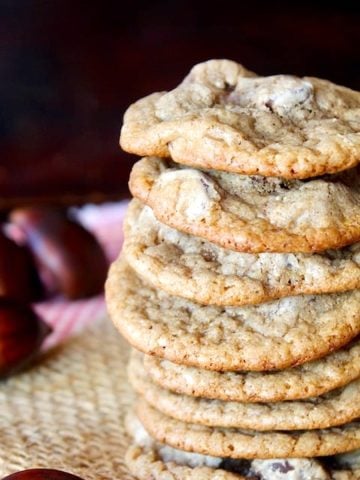 Tall stack of Chestnut Cookies with chocolate chips on raw chestnuts next to them