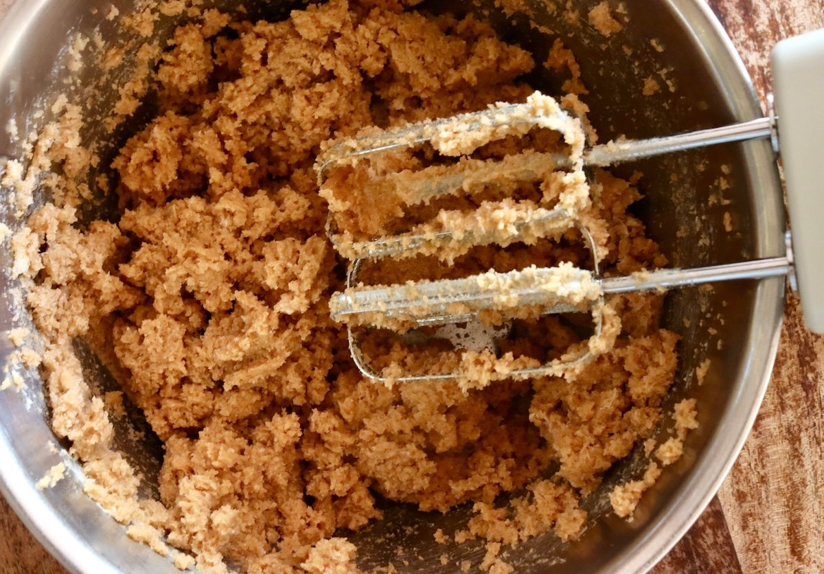 Stainless steel bowl with the beginning of chestnut cookie batter with sugar and butter blended, and two electric beaters.