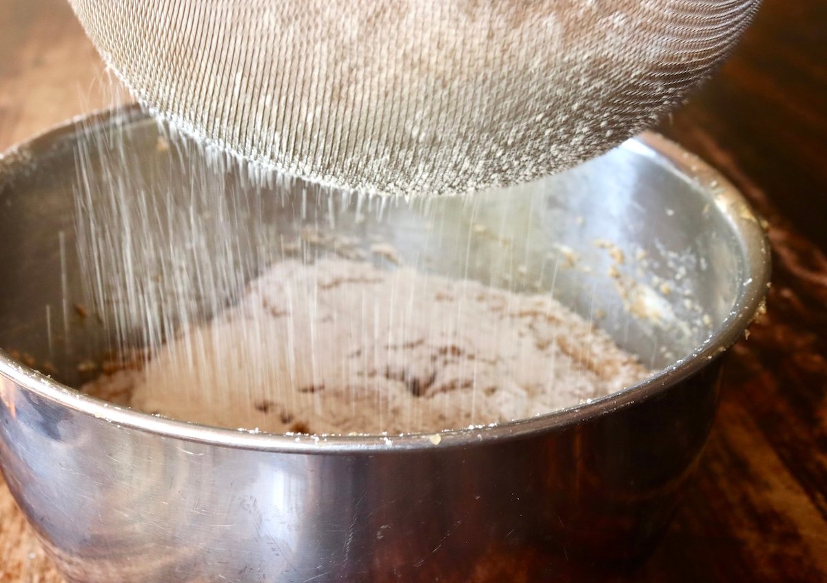 Chestnut flour being sifted into a stainless steel bowl.