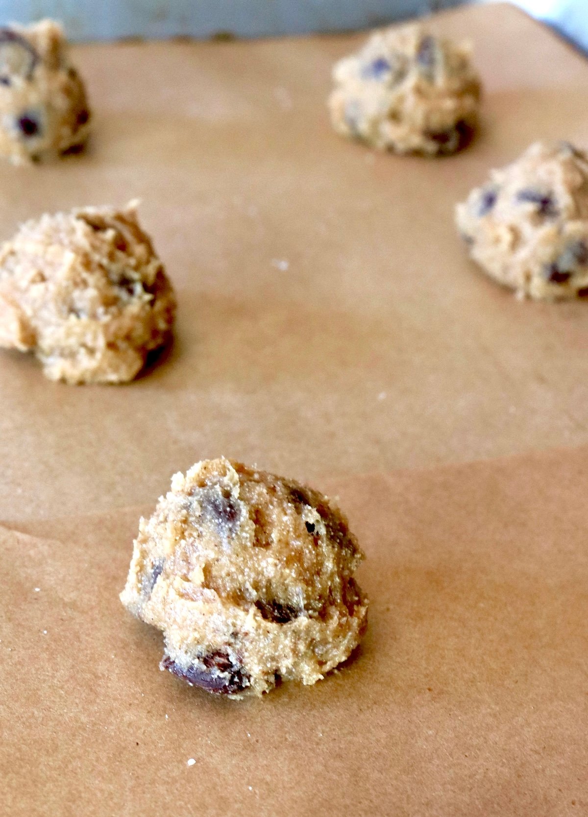 Balls of chestnut chocolate chip cookie dough on parchment paper-lined baking sheet.