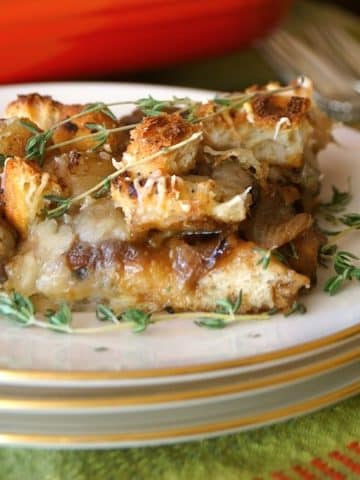 One square slice of French Onion Mushroom Casserole on white plate with red casserole pan in back.