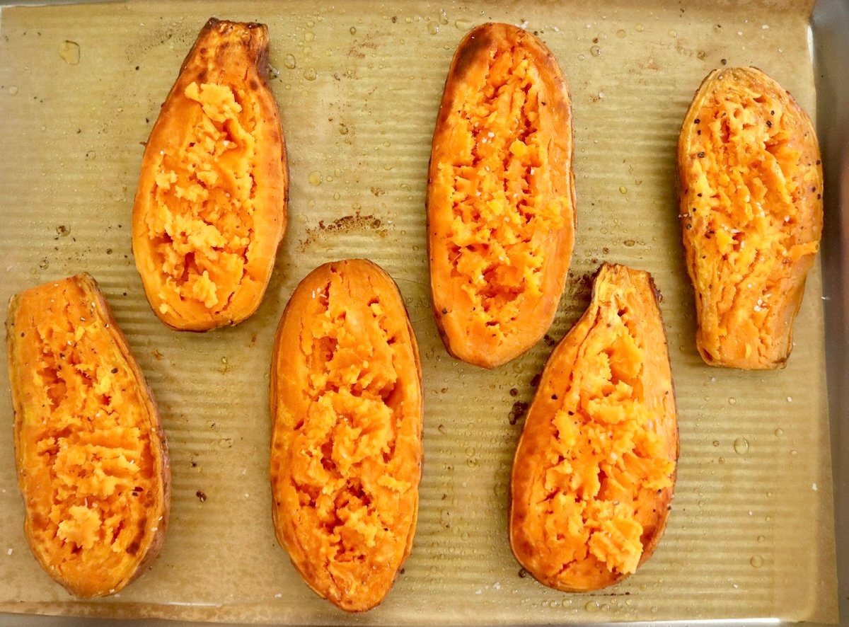 Six halves of orange sweet potatoes, flesh side up on a parchment-lined sheet pan. 