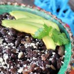 Cose up of black beans with avocado slices and cilantro in green rimmed bowl.