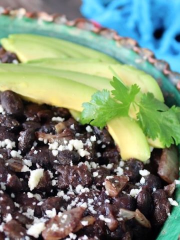 Cose up of black beans with avocado slices and cilantro in green rimmed bowl.
