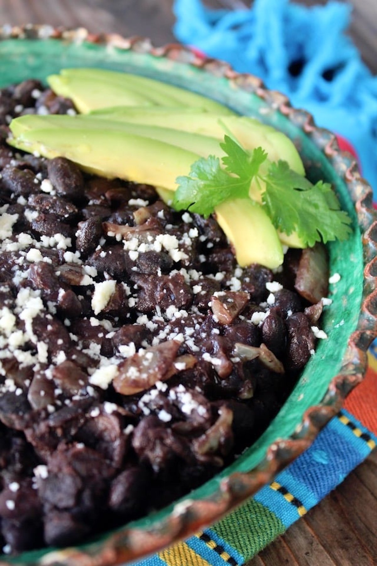 Mexican Black Beans made from scratch in green-painted terra cotta bowl with crimped edges.