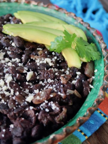 close up of black beans with avocado slices and cilantro in green rimmed bowl