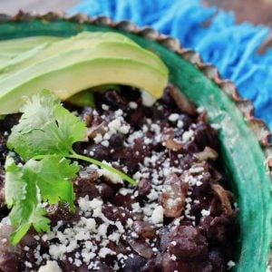black beans with avocado slices and cilantro in green rimmed bowl