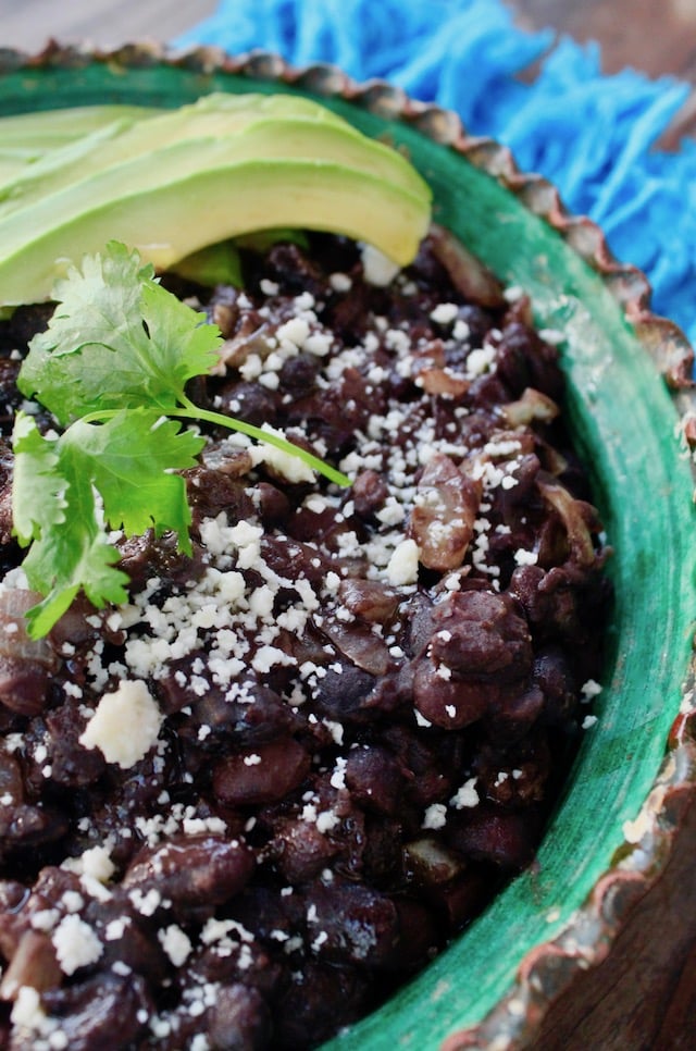 black beans with avocado slices and cilantro in green rimmed bowl