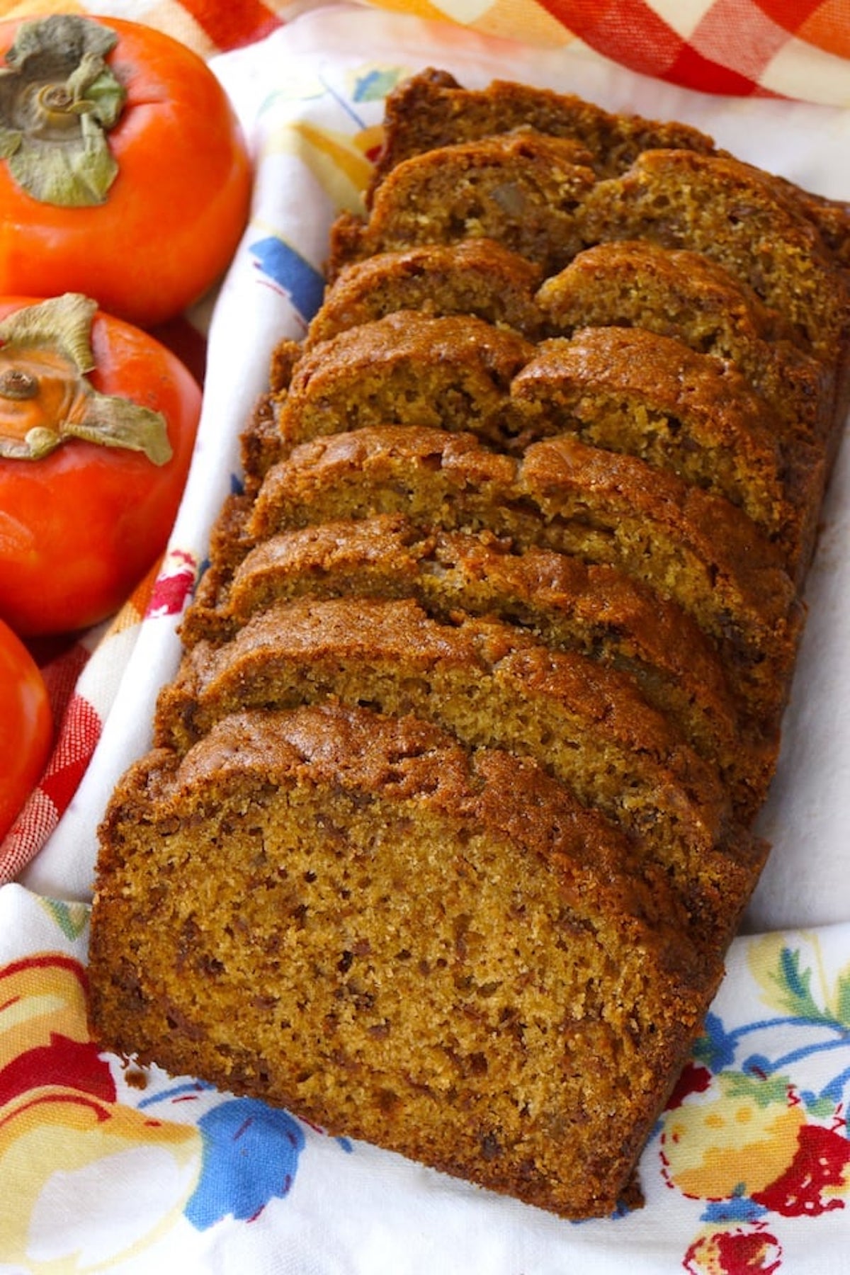 Sliced loaf of ginger persimmon bread with 3 whole persimmons next to it.