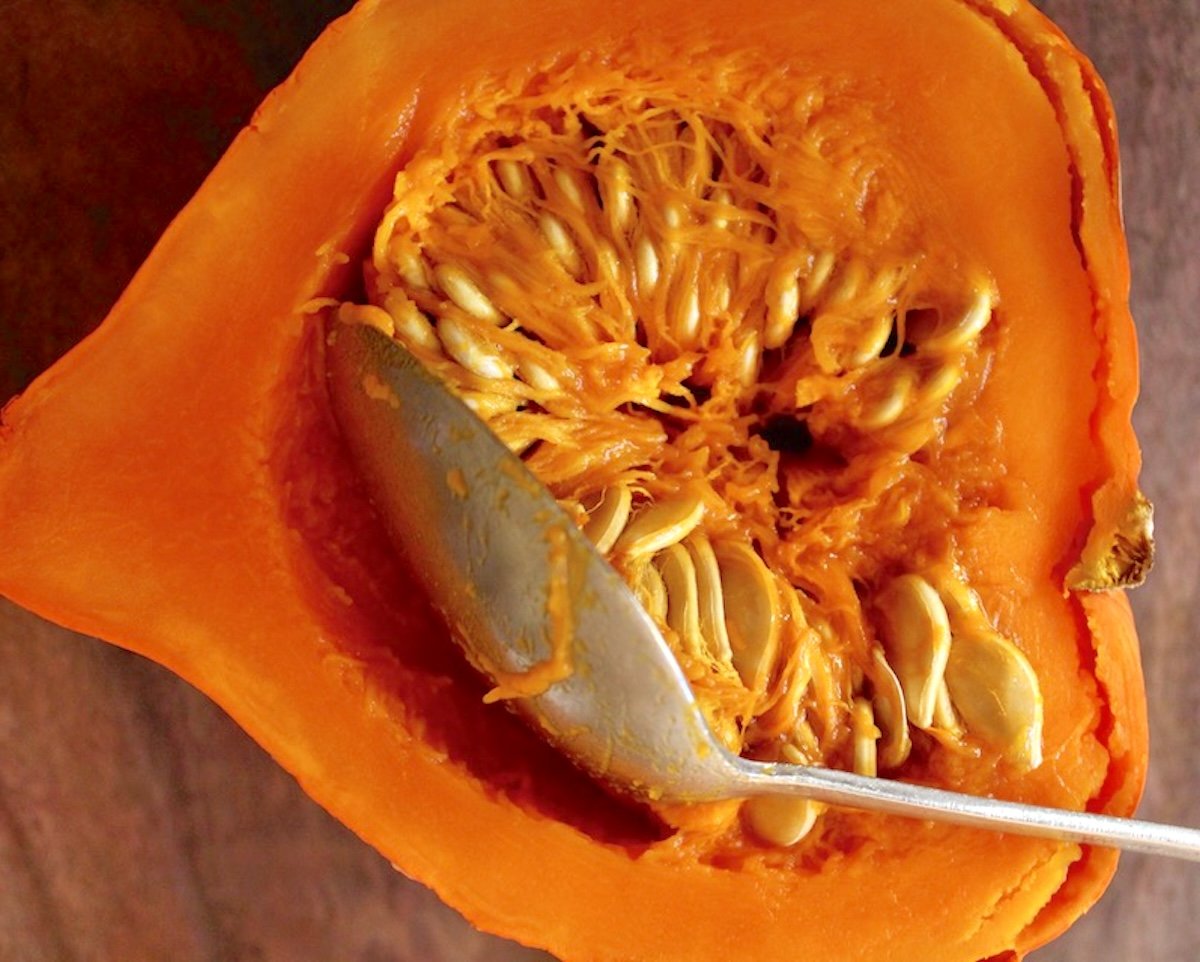 Roasted Red Kuri squash with seeds being removed with a stainless steel spoon.