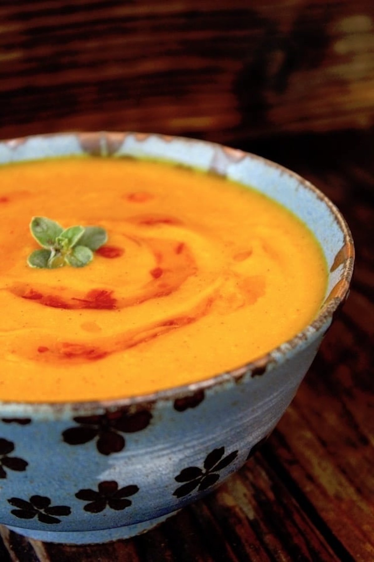 Bright orange Red Kuri Squash pureed soup, in a blue bowl with a small oregano leaf on top.