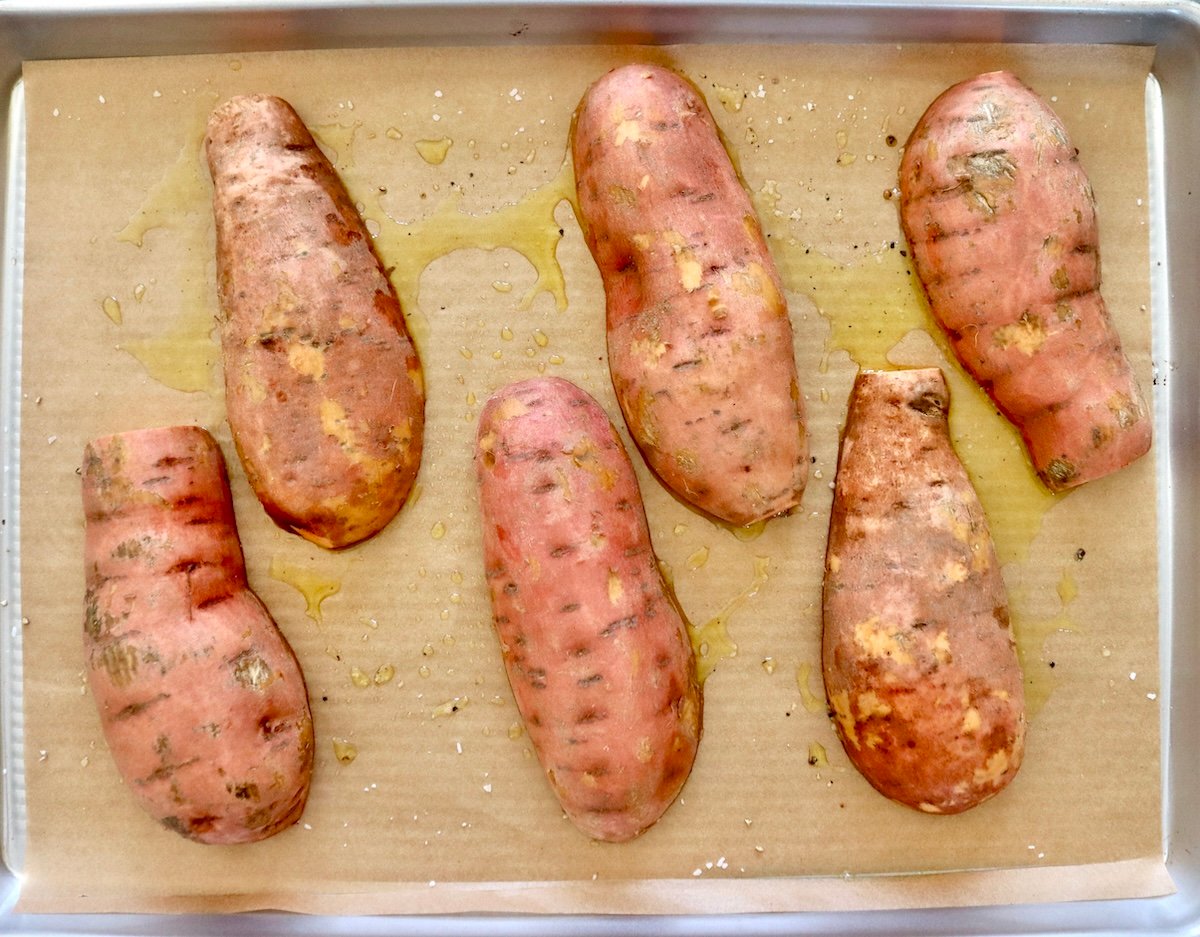 Six halves of orange sweet potatoes, round side up on a parchment-lined sheet pan. 