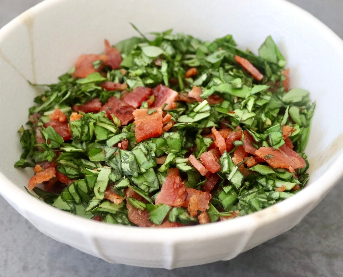 Small white bowl with chopped cooked bacon and finely chopped fresh basil.