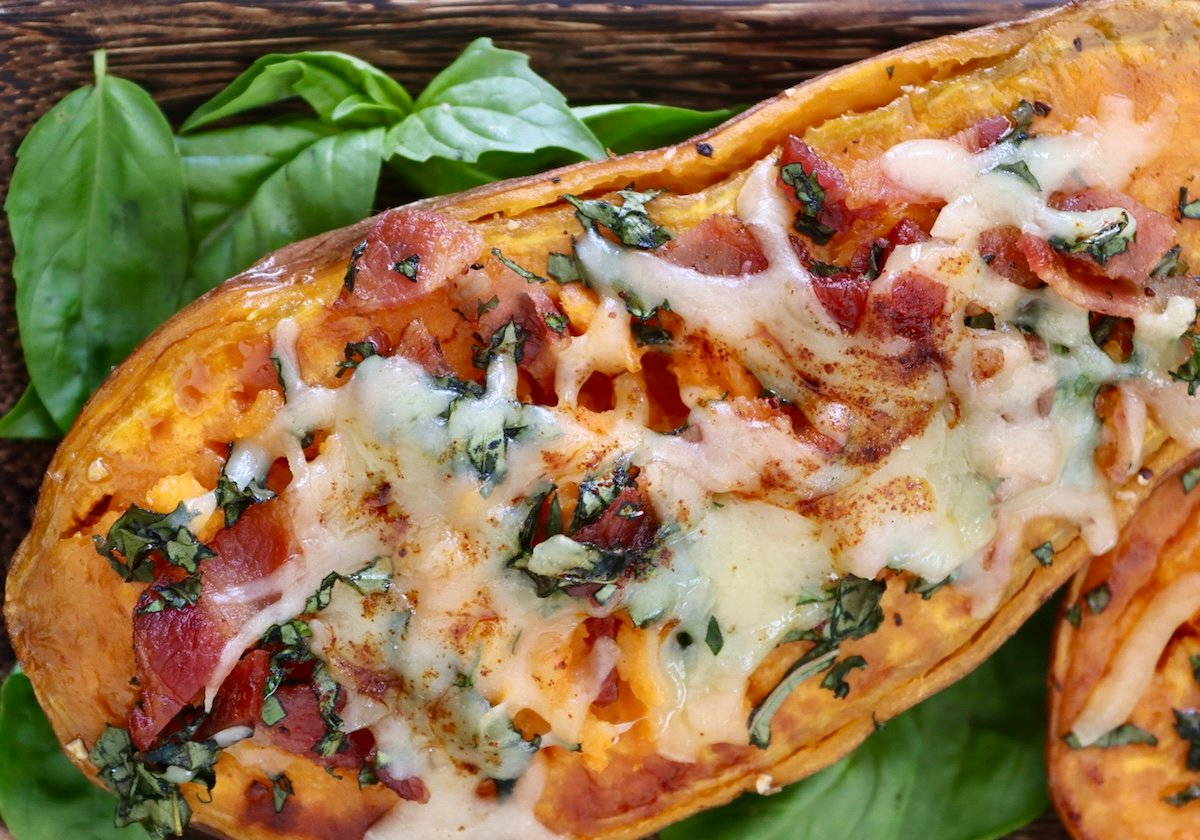 One baked sweet potato half with bacon, basil and melted cheese on top.